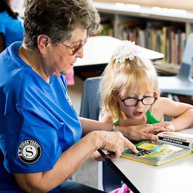 Older woman teaching a young child how to read in a classroom.